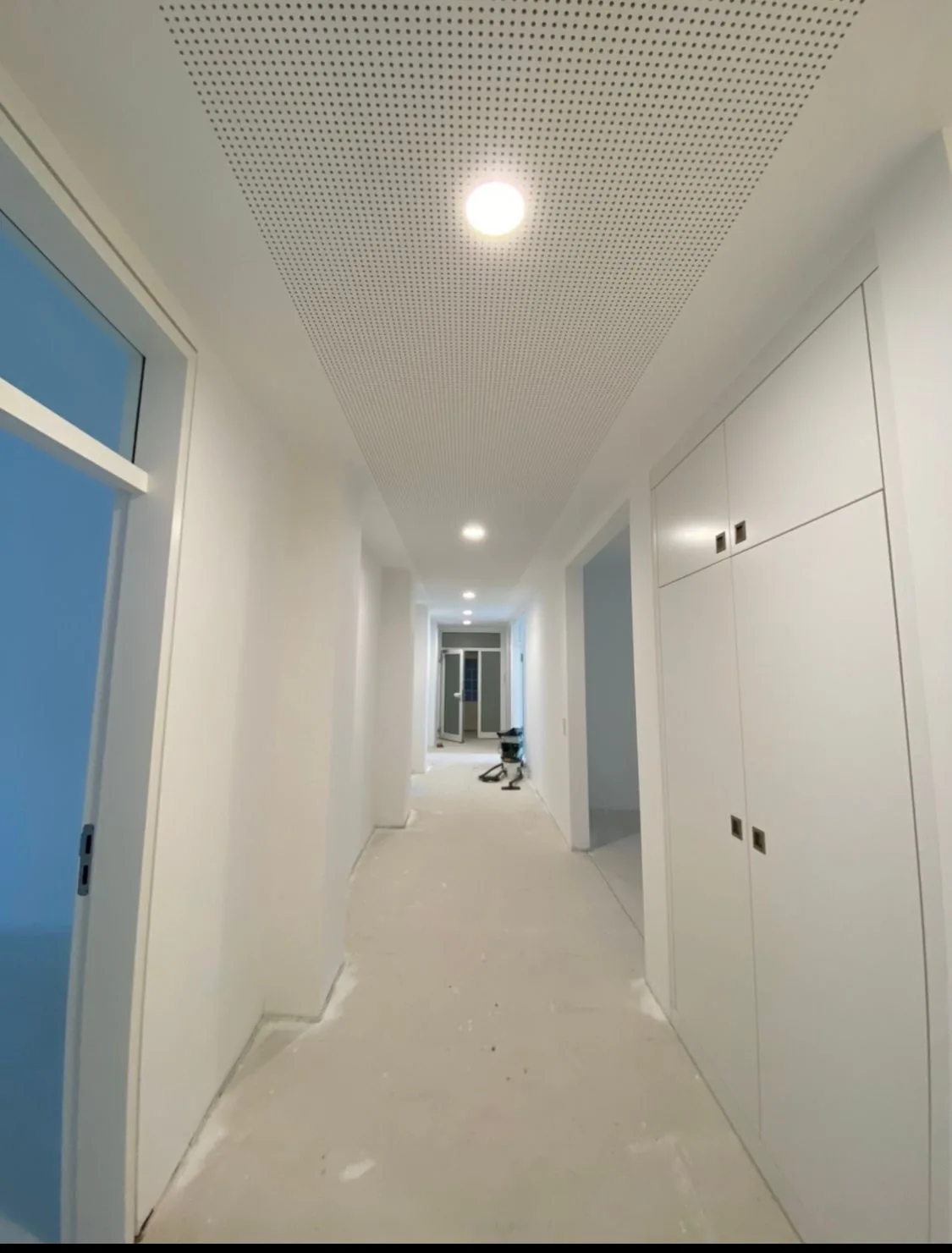 Flur mit abgehängter Gipskarton-Lochdecke: die feine Lochung absorbiert den Schall, eingelassene Leuchten sitzen bündig in der Fläche.