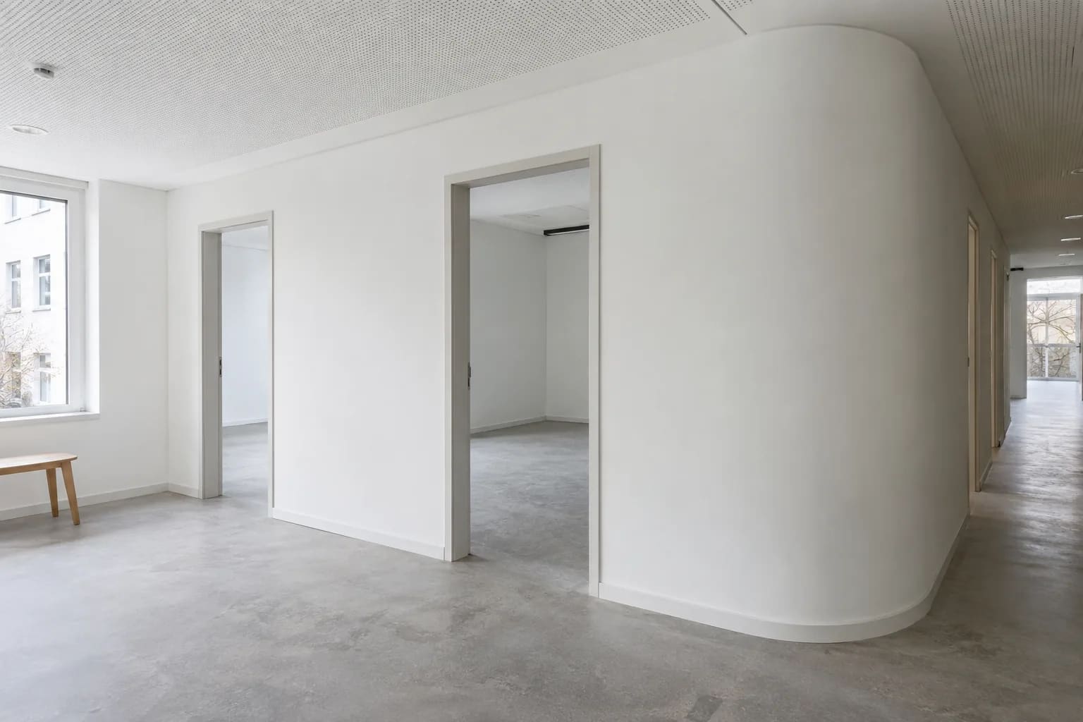 Geschwungene Trockenbauwand in einem Flur, fugenlos gespachtelt, mit bündig eingesetzten Türöffnungen und Akustikdecke darüber.
